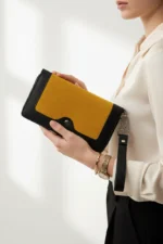 Black and yellow clutch purse with a wrist strap held by a person wearing a watch