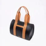 Black leather duffel bag with tan leather straps and accents on a white background