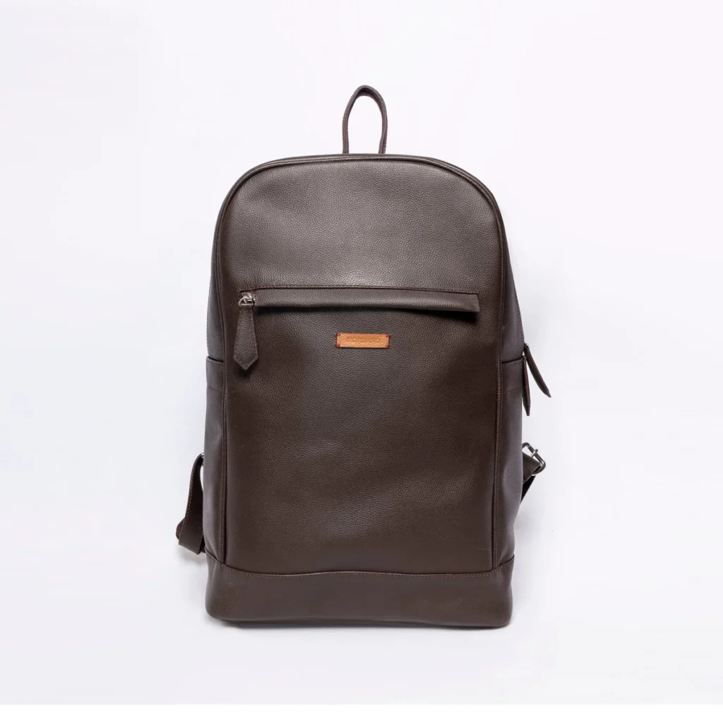 Brown leather backpack with a front zipper pocket and a small orange logo tag