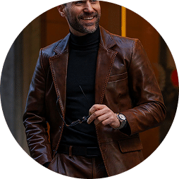 Man wearing a brown leather jacket and matching pants, holding glasses
