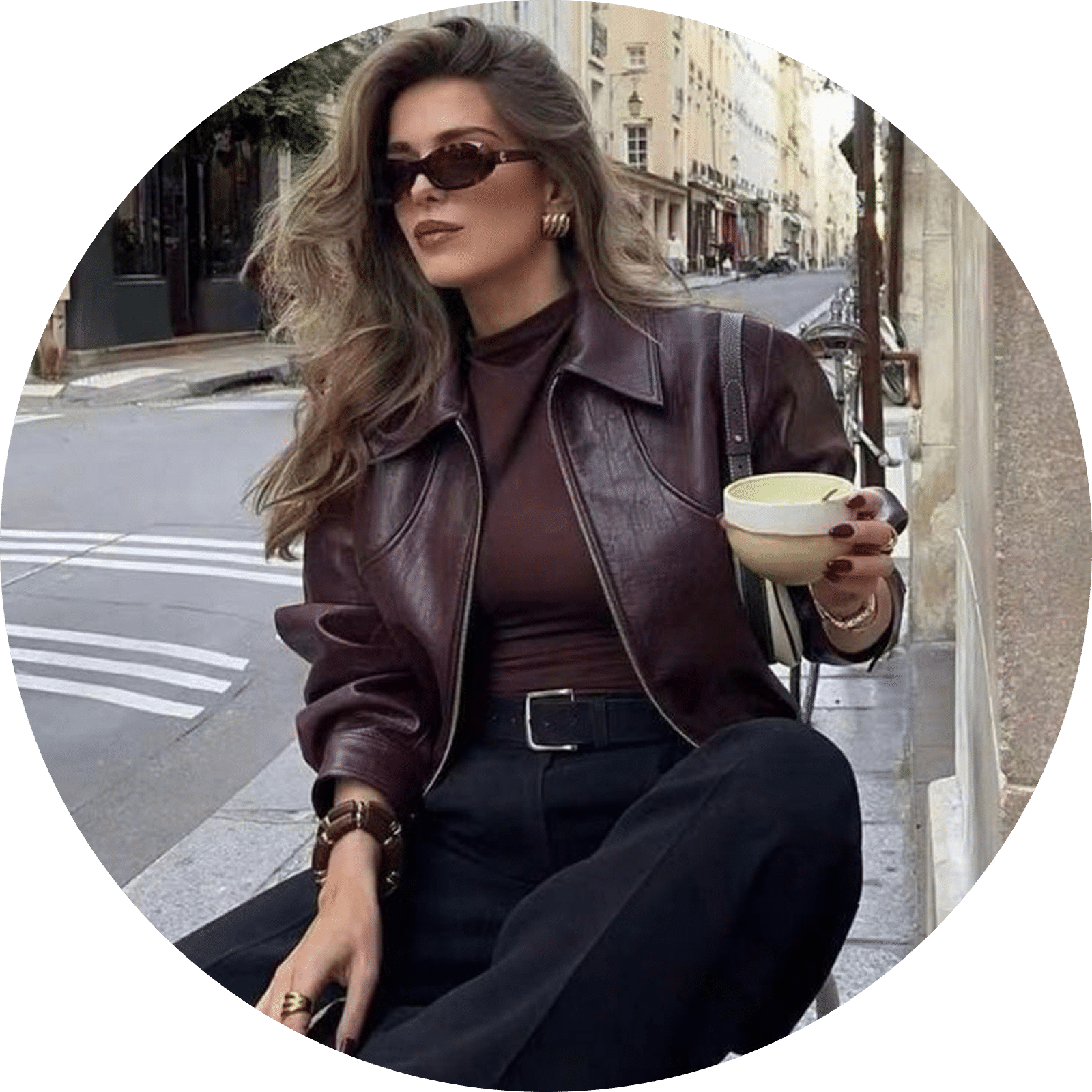 Woman in a burgundy leather jacket and dark pants holding a cup outdoors