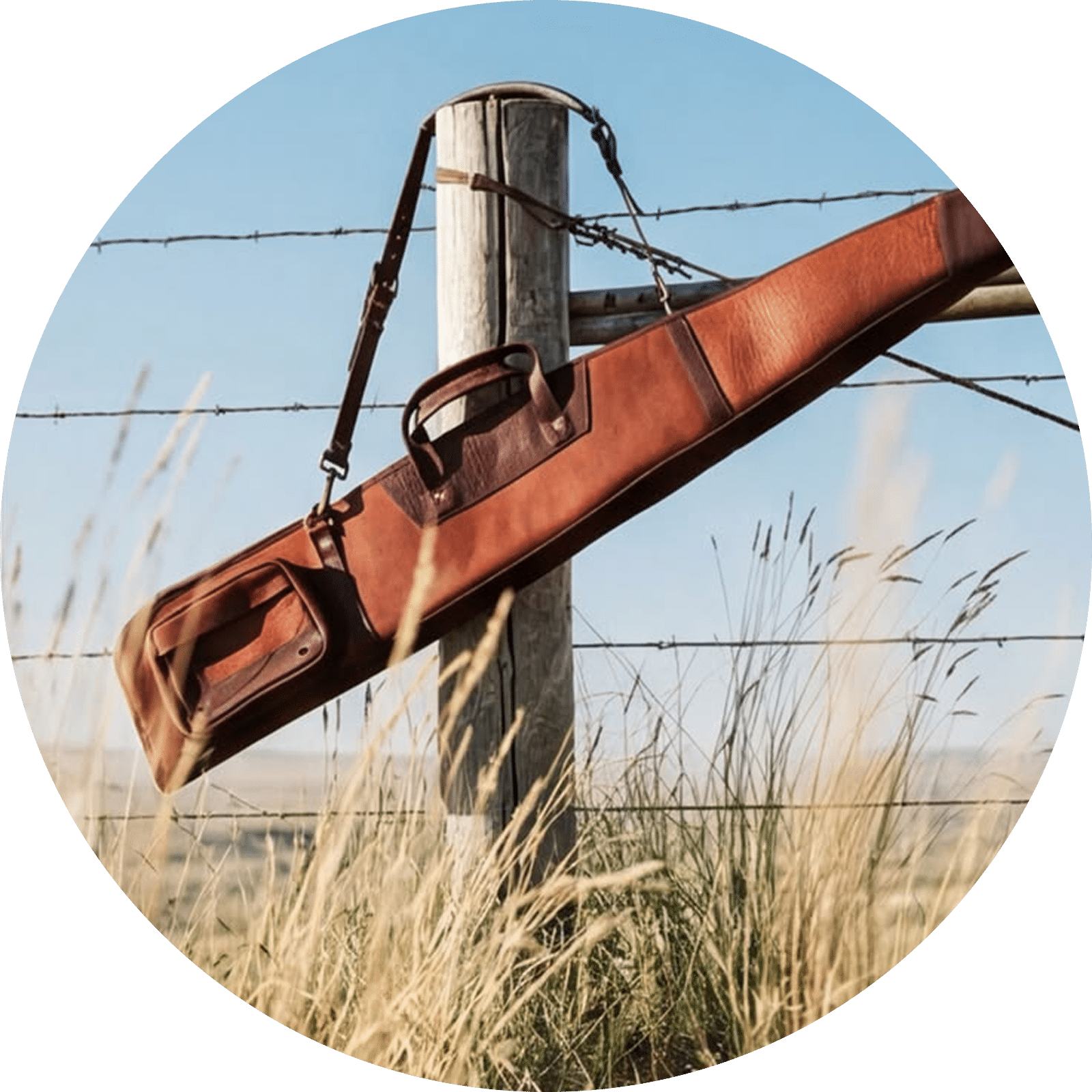 Brown leather gun case with straps hanging on barbed wire fence post outdoors