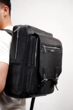 Black leather backpack with buckle and zipper closures, worn by a person